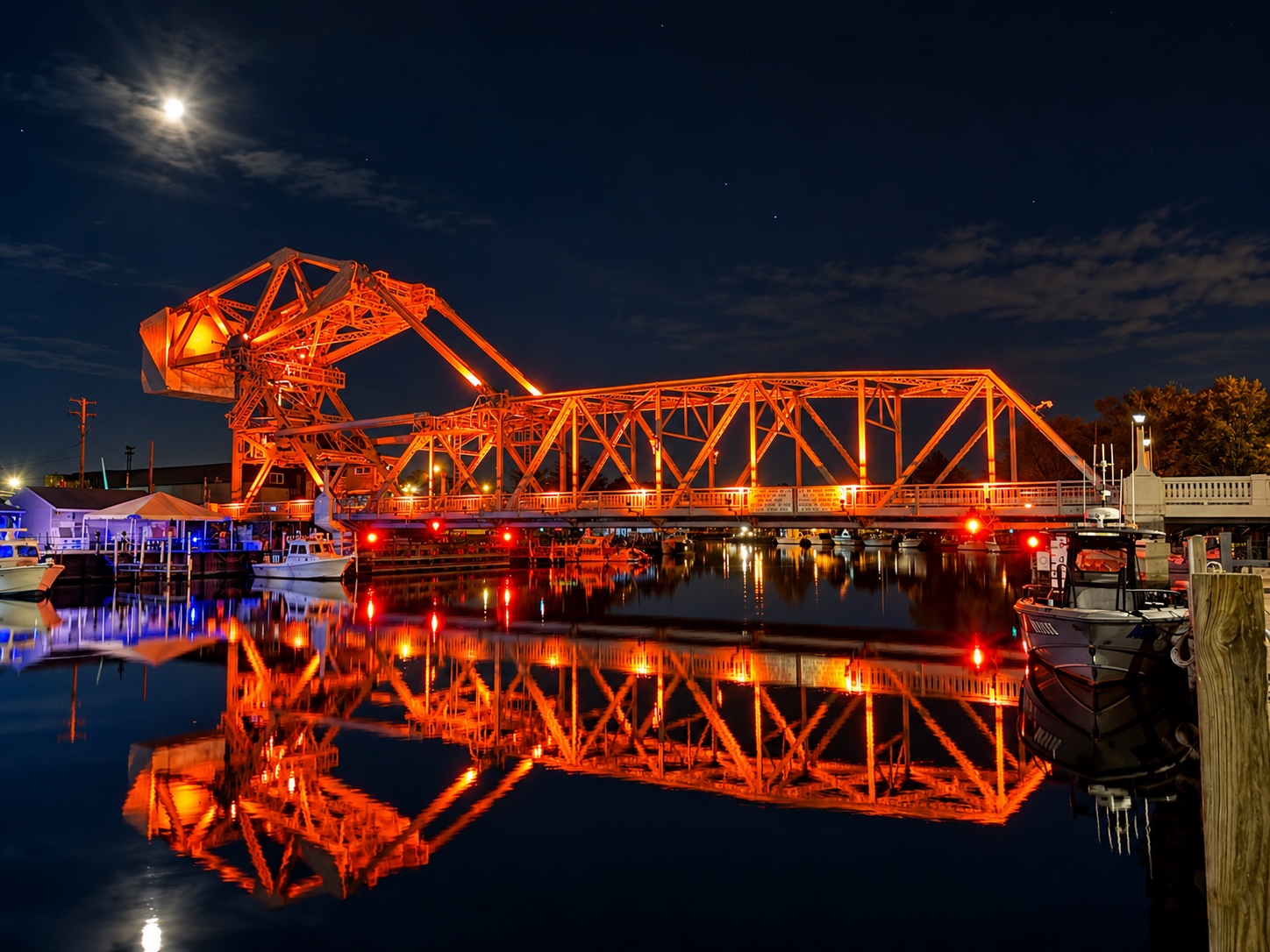 Ashtabula Harbor lift bridge illuminated orange at night, reflected in the water beneath the moon